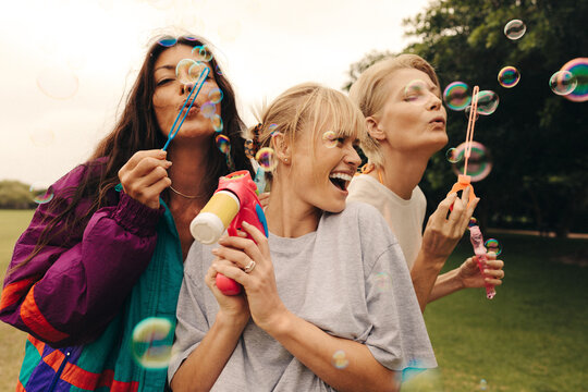 Three carefree female friends have fun blowing bubbles in a park