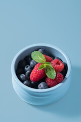 Raspberries with blueberries in a blue cup on a blue background.
