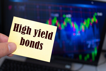 Male hand holding sticky note written high yield bonds.