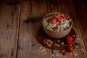 Oatmeal porridge with strawberries and nuts on dark wooden background