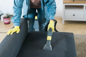 Cleaning service company employee removing dirt from furniture in flat with professional equipment....