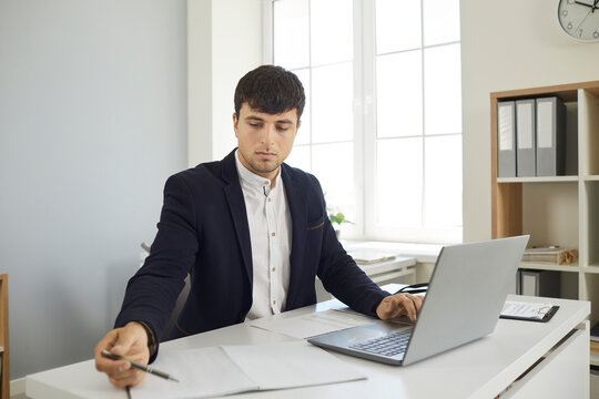 Business man on online meeting with clients writing making notes during conversation in laptop sitting at desk in office. Modern way of doing business, communicating customers online communication.