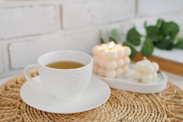 Cup of tea, book and white burning candles on table mat