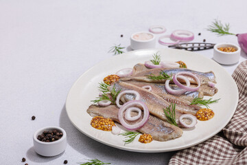 Salted herring with dijon mustard, dill and red onion rings on white stone background