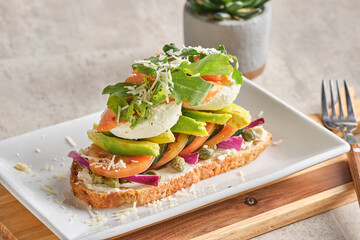 Closeup shot of bruschetta with poached eggs, avocado, tomatoes and onions arugula