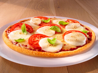 Pizza Tomate Mozzarella mit Basilikum auf weissem Porzellanteller