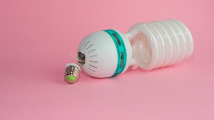 Broken energy saving lamp on a pink pastel background