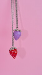 Red and a purple strawberry-shaped necklace on a pink background