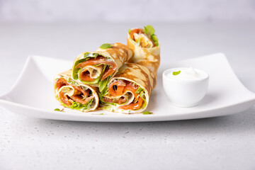 Pancakes with salmon (trout), sour cream and greenstuff. Thin, not sweet blinchiki stuffed with red fish. Traditional Russian and Ukrainian dish. Feast of Maslenitsa. Selective focus, close-up.