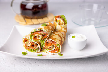 Pancakes with salmon (trout), sour cream, greenstuff and tea. Thin, not sweet blinchiki stuffed with red fish. Traditional Russian and Ukrainian dish. Feast of Maslenitsa. Selective focus, close-up.