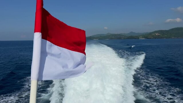 Travel Indonesia. Red and white national flag of Indonesia winding in the wind on a fast boat moving along blue ocean with distant island. Soft focus. Film grain pixel texture. Live camera. Blur.