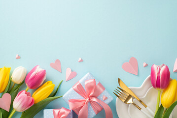 Spring Mother's day table setting. Top view flat lay of plates, cutlery, tulips, gift boxes, and decorative hearts on pastel blue background with empty space for text or advert