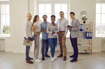 Group portrait of happy successful business people at work in the office. Team of six diverse company employees standing in a modern office and smiling. Full body length indoor shot