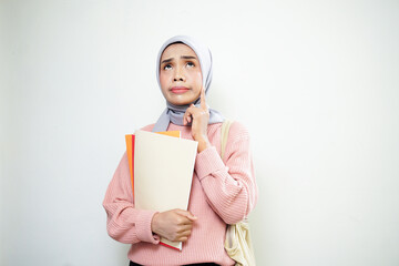 Smiling Asian Muslim female student in pink sweater with medium bag, holding book and thinking isolated on white background. back to school concept