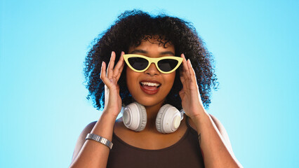 Trendy black woman face isolated on blue background for beauty, cosmetics and fashion of gen z lifestyle. Confident african american person or model with cool sunglasses and headphones for summer