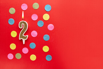 Number 2 on a red background with colored confetti. Happy birthday candles. The concept of celebrating a birthday, anniversary, important date, holiday. Copy space. banner