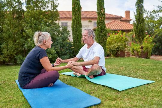 Happy senior couple holding hands on yoga mats in villa garden