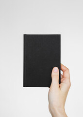a woman's hand holds a small book in a black cover