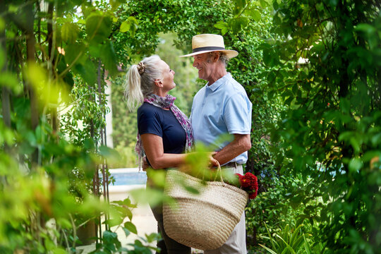 Happy senior couple hugging under lush green trellis in summer garden - Powered by Adobe