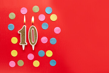 Number 10 on a red background with colored confetti. Happy birthday candles. The concept of celebrating a birthday, anniversary, important date, holiday. Copy space. banner
