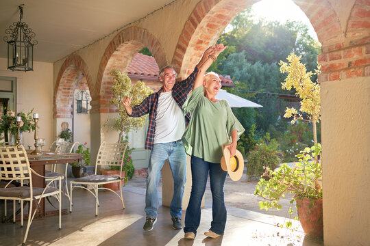 Happy, carefree senior couple dancing on sunny villa patio