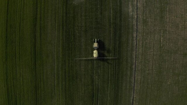Aerial drone footage of a tractor fertilizing a green crop field