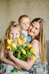 Mom, son and daughter smiling and hugging. Mother's day concept. Girl and boy congratulates mother and gives a bouquet of flowers tulips at home. Holiday greeting card for International Women's Day.