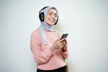 Smiling Asian Muslim female student in pink sweater with bag and cellphone listening to music isolated on white background. back to school concept