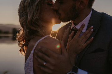 Closeup shot of the bride and the groom kissing on the sunset background