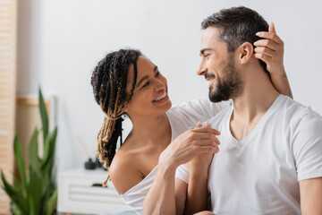 joyful african american woman and bearded man smiling at each other in bedroom at home.