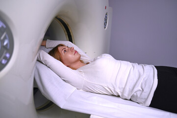 A young woman is undergoing a CT scan procedure. Pretty female in a modern laboratory, lying on the table during CT or MRI. 