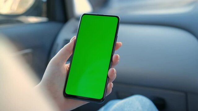 Slow motion woman hands holding touch a smartphone with vertical green screen in car sunshine driver automobile display communication internet message navigation park traffic transport close up