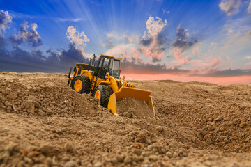 Wheel loader are digging the soil in the construction site on  sunset background.