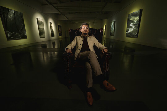 Old artist inside the gallery sitting on sofa