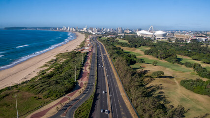 Fototapeta na wymiar A drone view of the freeway into the city of Durban, with sea and beach on one side and the golf course and the Moses Mabhida Stadium on the other. 