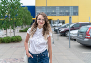 Fototapeta premium Beautiful Young Caucasian Woman is Leaving Shopping Mall. Parking Lot in Background.