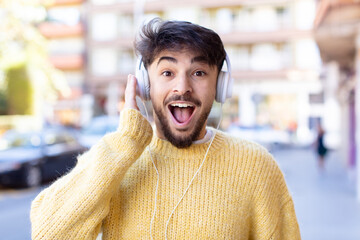 young handsome man feeling happy and astonished at something unbelievable. listening music with headphones