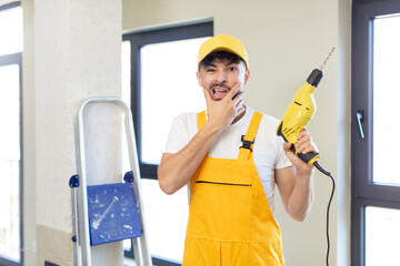 young handsome man with mouth and eyes wide open and hand on chin. handyman and drill concept