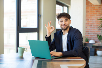 Fototapeta premium young handsome man feeling happy, showing approval with okay gesture. freelance concept with laptop