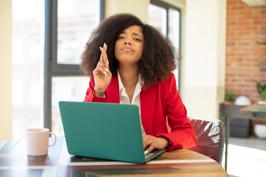 pretty afro black woman crossing fingers and hoping for good luck. businesswoman and laptop concept