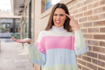 pretty young adult woman feeling confused and puzzled, showing you are insane, crazy or out of your...