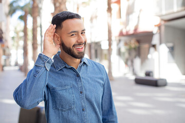 young handsome man looking happy, listening, trying to hear a secret conversation or gossip,...