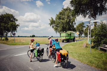Familie auf einer Fahrradtour durch Niedersachsen in den Sommerferien wartet an einer Straßenkreuzung, an der eine Landmaschine vorbei fährt, Deutschland