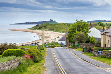 View down the hill to the sandy beach at Low Newton-by-the-Sea in Northumberland, with Dunstanburgh...