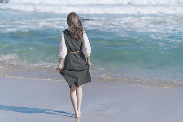 秋の季節に綺麗な海の波打ち際を裸足で歩く女性
