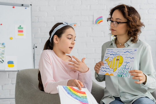 Preteen child talking while psychologist holding drawing in consulting room.