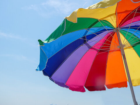 A large opened multi - colored beach umbrella against a blue sky