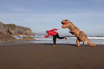 T-rex  runs after a man on the ocean beach in Zumaia, Spain. Dinosaur runs after a man next to sea.