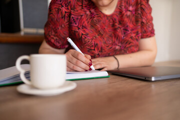 Close up photo of woman writing in her notebook while working from home.