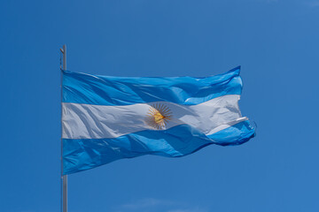 The national flag of the Argentine Republic with blue sky and white clouds in the background. 